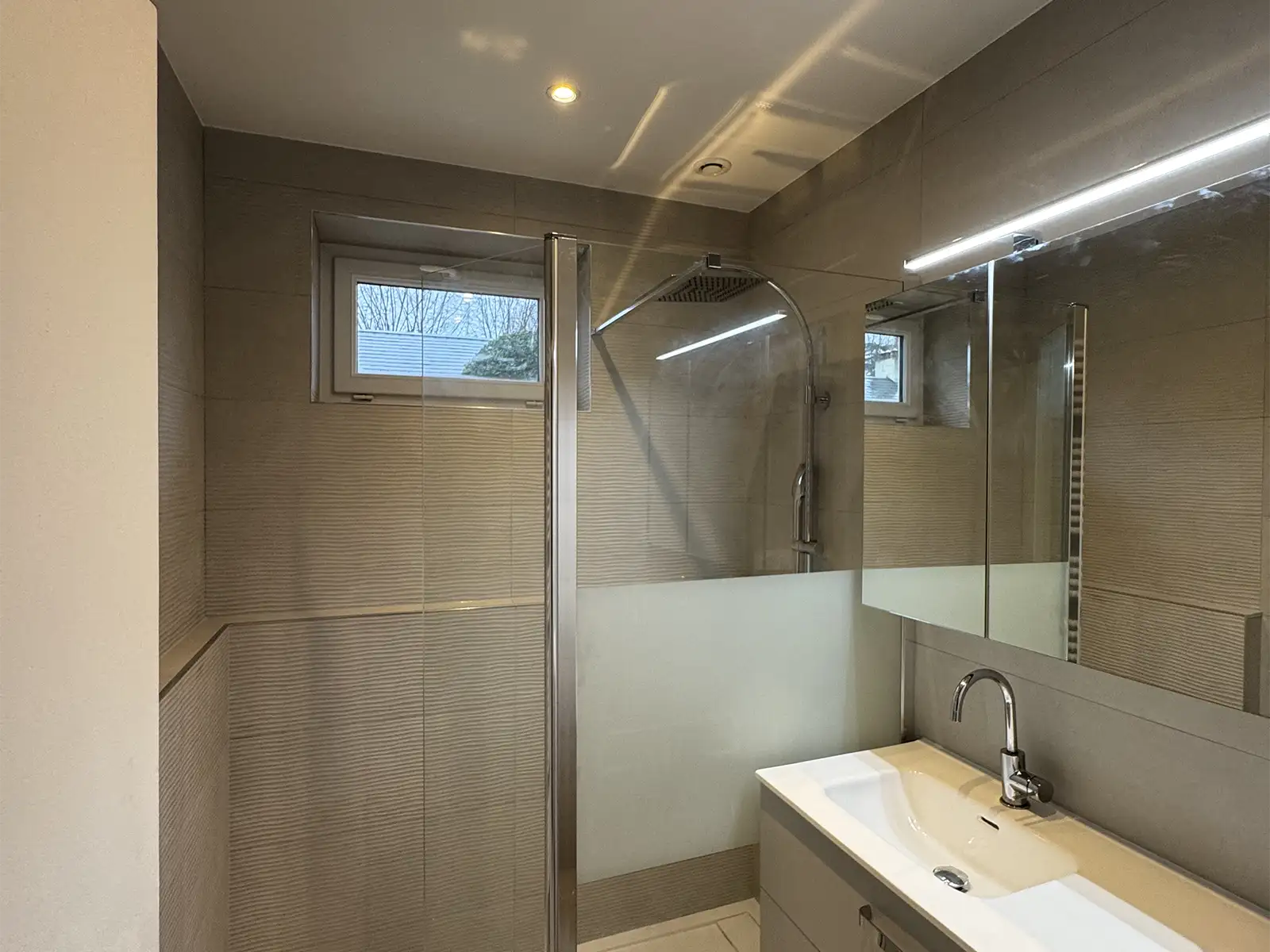 Salle de bains rénovée avec carrelage gris effet pierre au sol et murs, parement imitation marbre, douche à l’italienne, meuble suspendu blanc et robinetterie encastrée inox Saint Michel Sur Orge (91570)