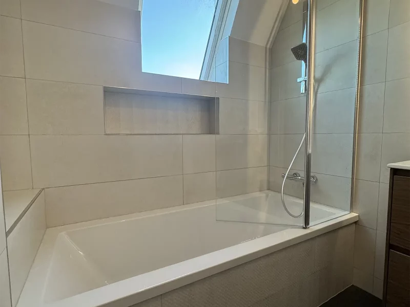 Douche avant rénovation avec carreaux blancs simples, rangement encastré dans le mur et pommeau de douche en inox fixé au mur