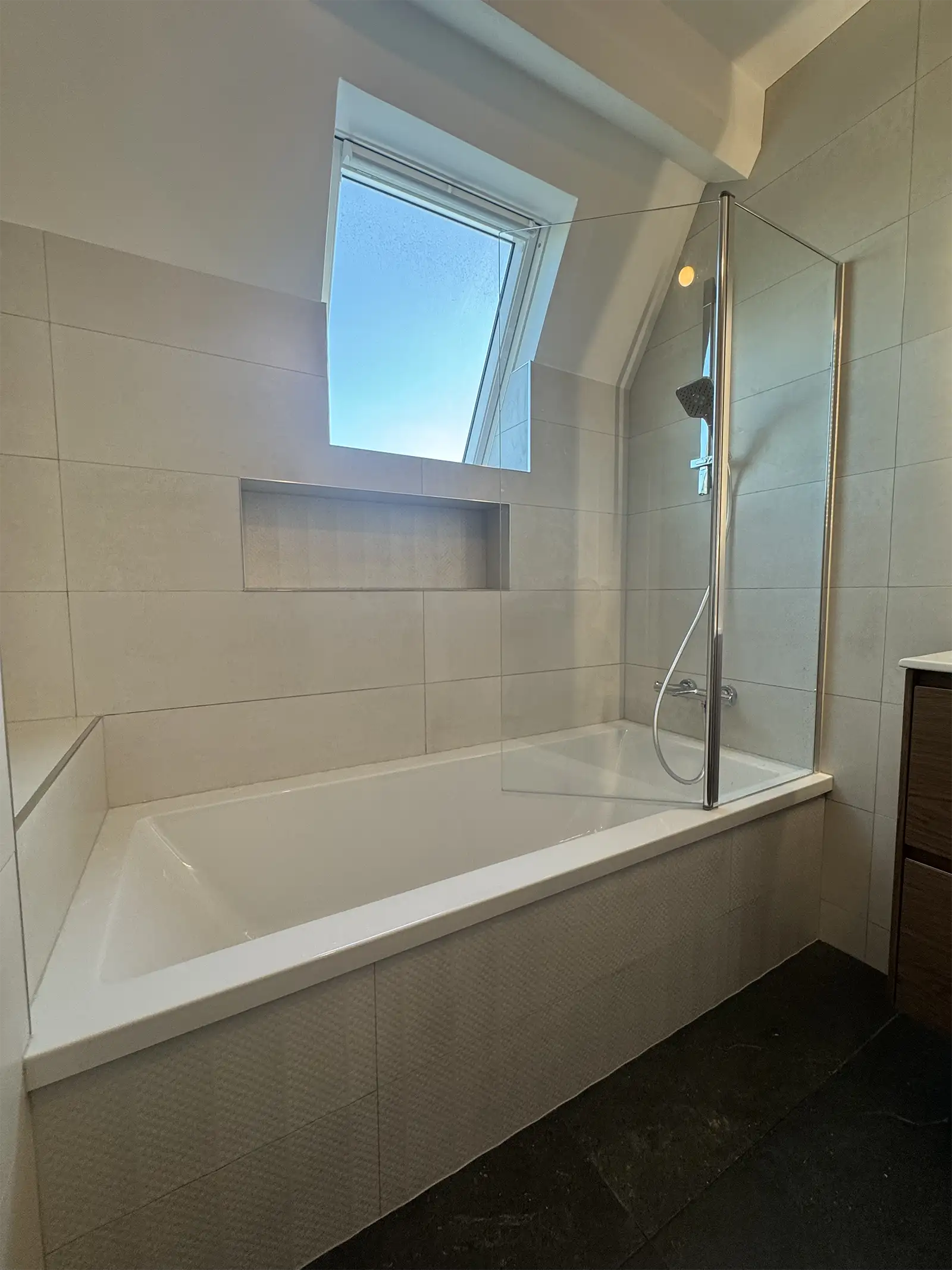 Douche avant rénovation avec carreaux blancs simples, rangement encastré dans le mur et pommeau de douche en inox fixé au mur