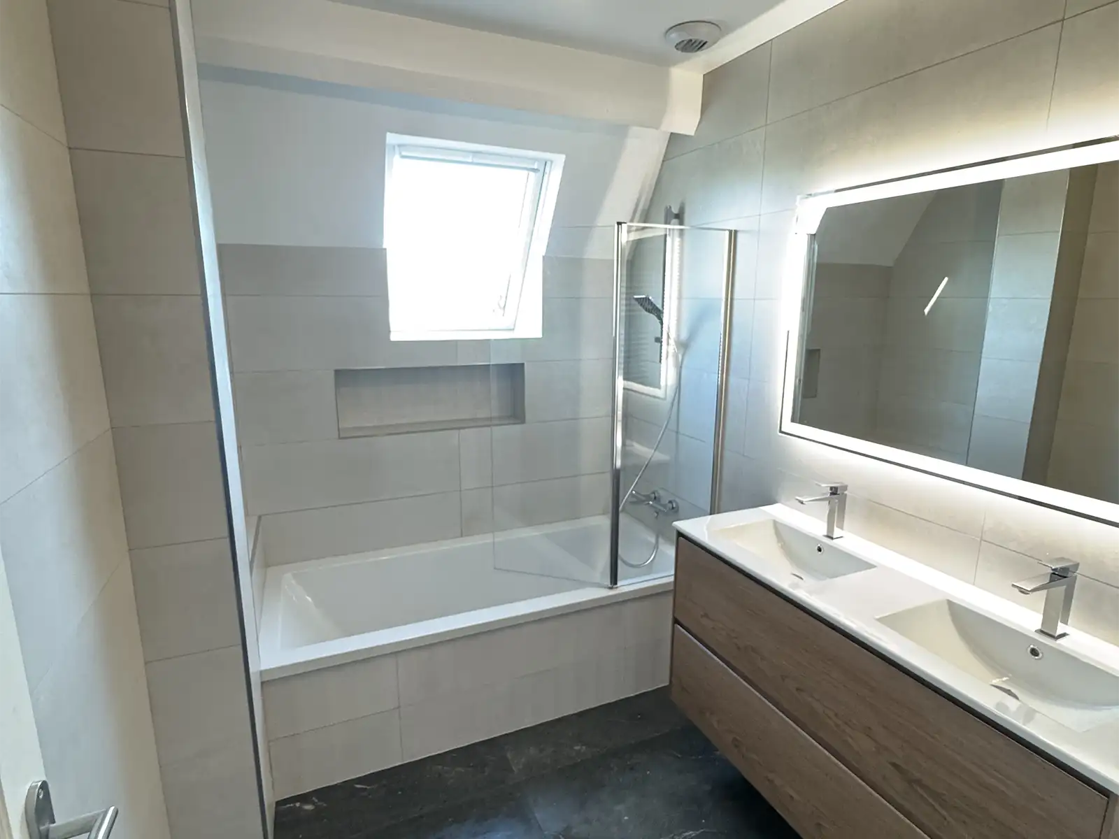 Salle de bains après rénovation avec paroi vitrée de douche à l’italienne, miroir carré à LED, vasque encastrée dans meuble en bois et robinet en inox