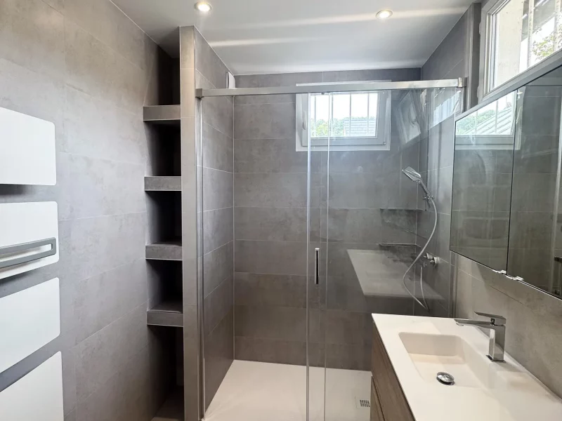 Salle de bains gris perle minimaliste à Orsay avec douche vitrée, sèche-serviettes blanc et mobilier double vasque bois à Orsay(91)