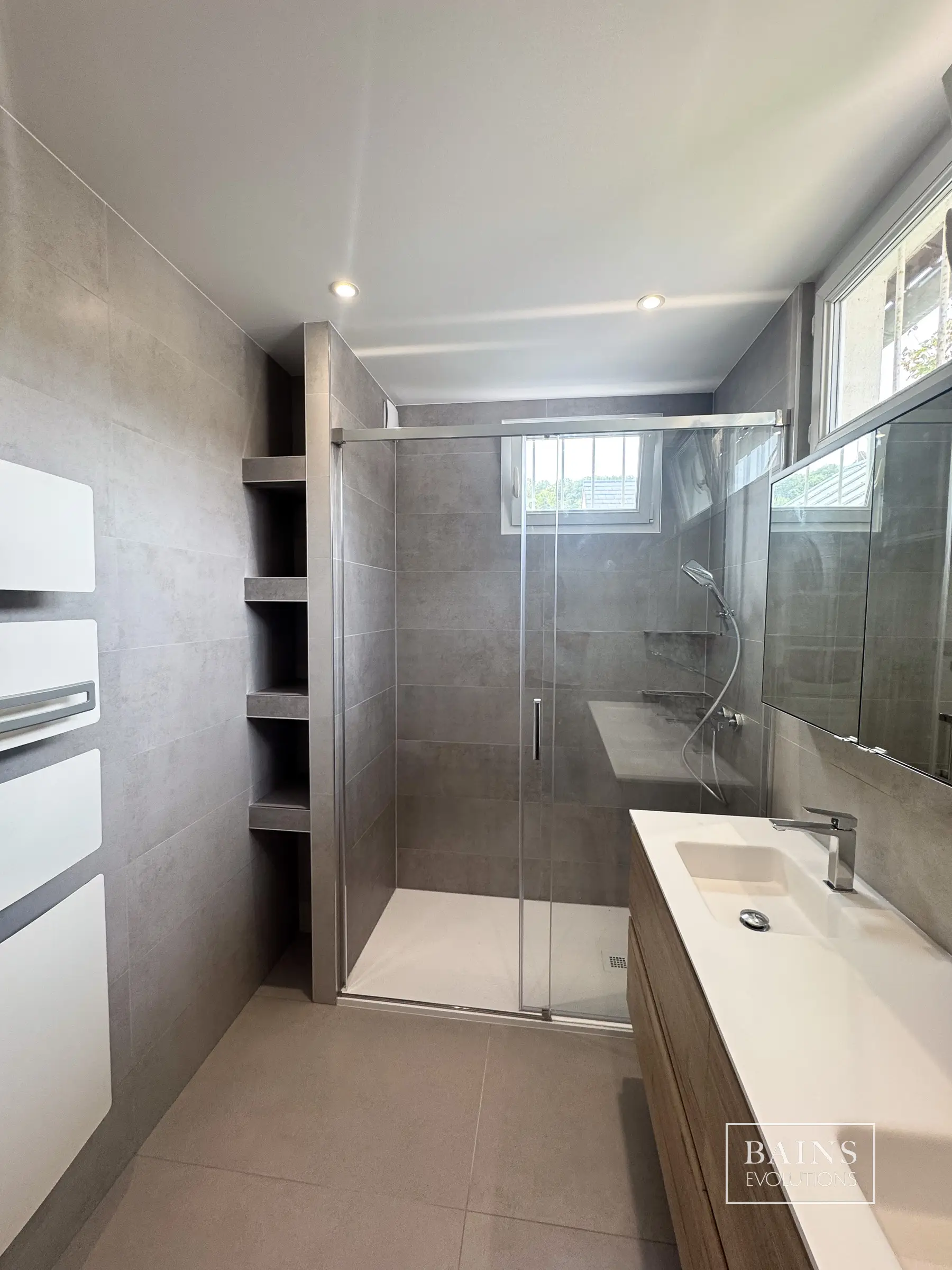 Salle de bains gris perle minimaliste à Orsay avec douche vitrée, sèche-serviettes blanc et mobilier double vasque bois à Orsay(91)