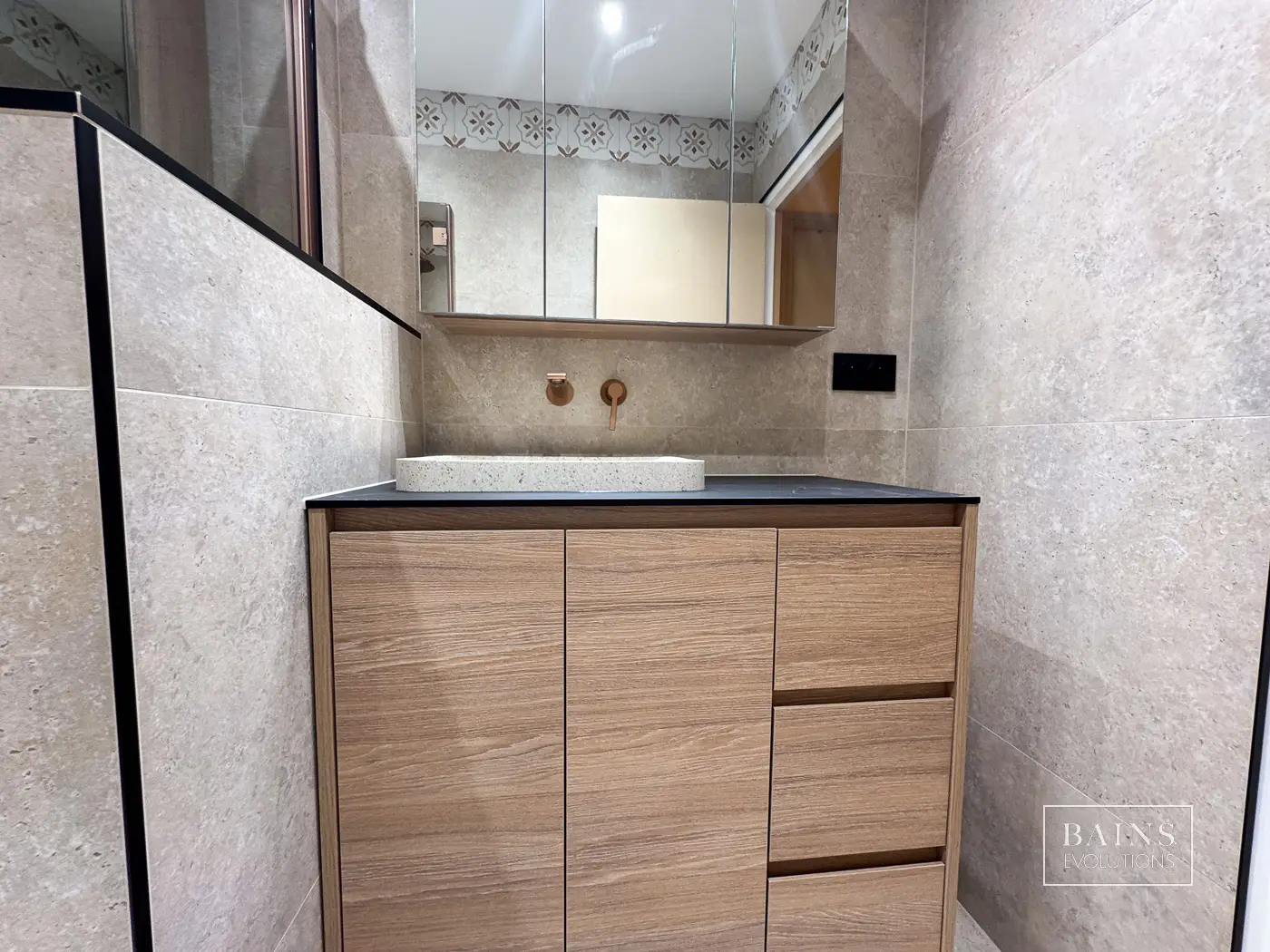 Salle de bains en travertin ivoire avec meuble KYRYA effet bois et finitions cuivre brossé à Marcoussis (91)